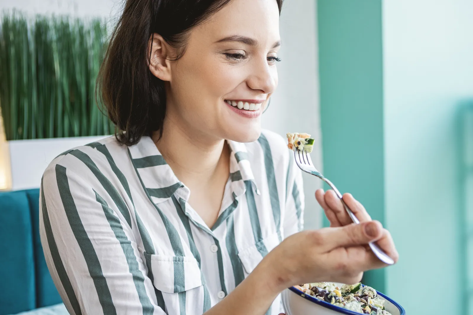 Woman smiling as she eats a fresh salad from a bowl