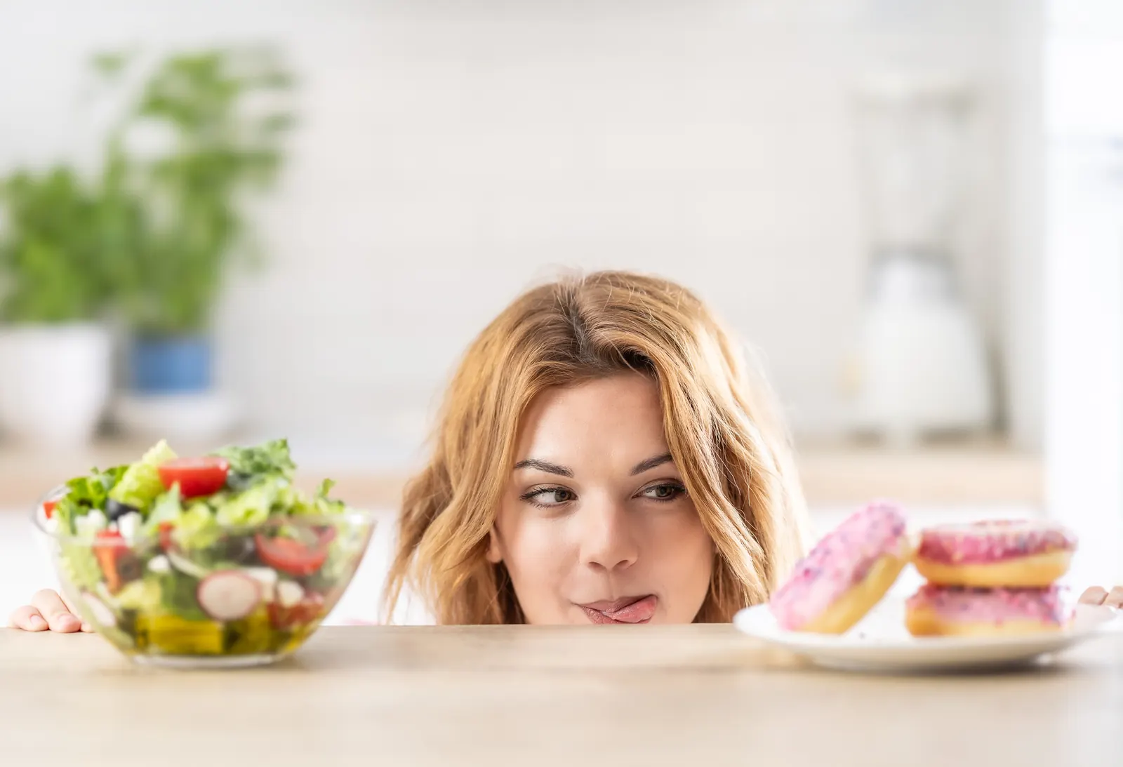 Woman looking at a salad next to a plate of doughnuts