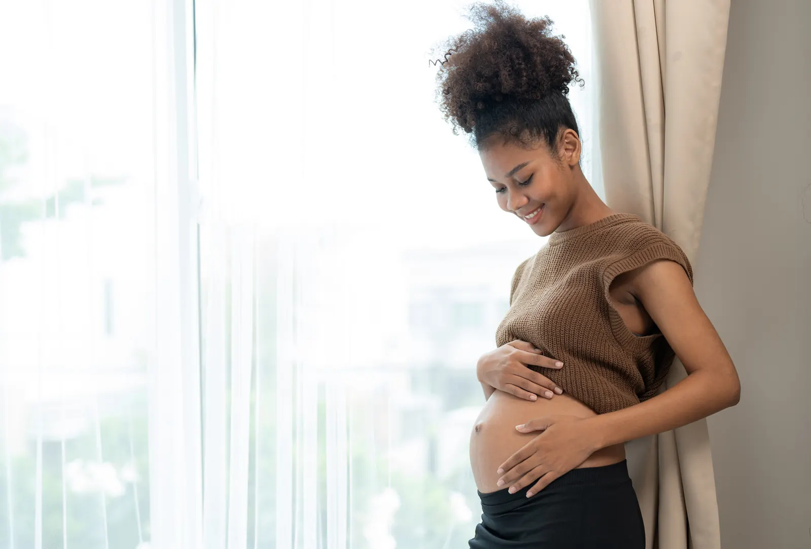 Pregnant woman standing by a window holding her bump